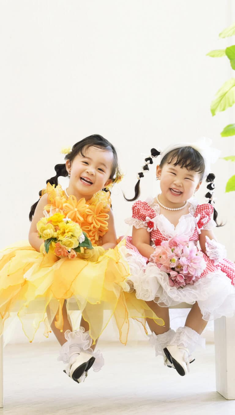 黄色と赤の華やかなドレス。ブーケを手にして笑う二人の姉妹