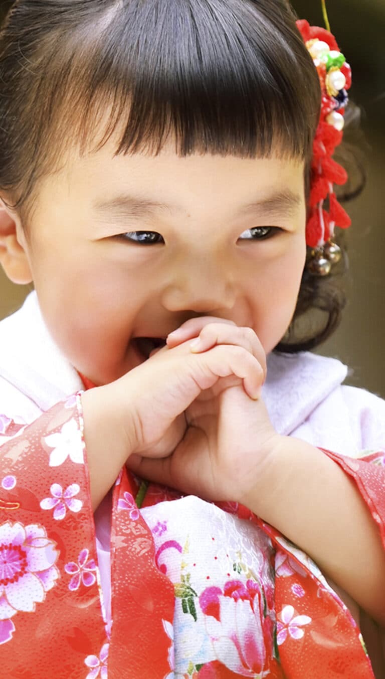 赤地に桜や菊の花柄の着物。口元に手を当てて笑う女の子